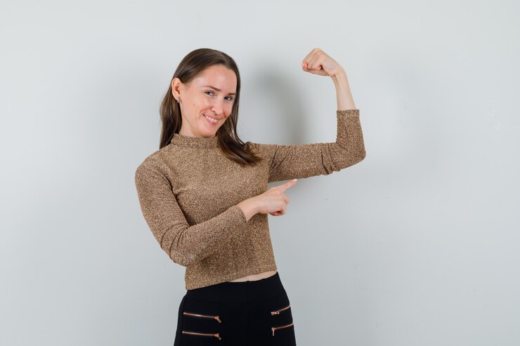 Foto gratuito mujer joven en blusa, falda apuntando al músculo del brazo y mirando feliz, vista frontal.