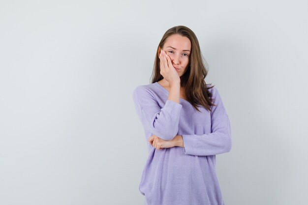 Mujer joven en blusa lila apoyando su mano con la palma abierta y con aspecto cansado