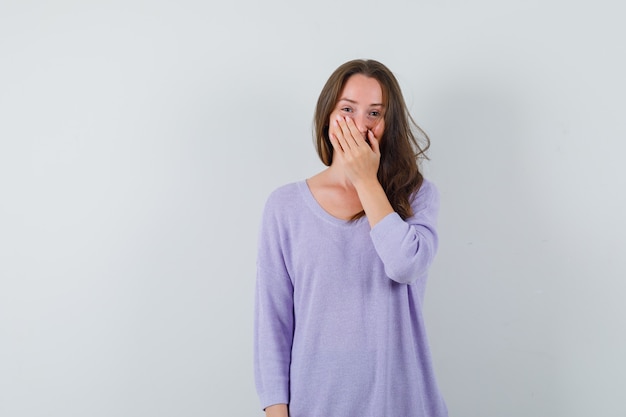 Mujer joven en blusa lila sosteniendo la mano en la boca y mirando complacido