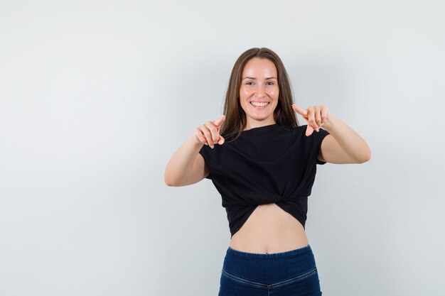 Foto gratuita mujer joven en blusa negra apuntando a la cámara y mirando alegre