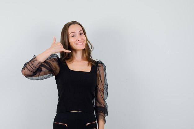 Mujer joven en blusa negra mostrando gesto de llamada telefónica y mirando complacido