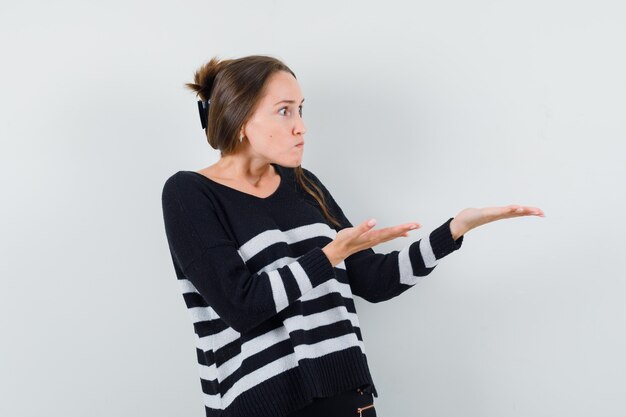 Mujer joven en blusa negra y pantalón negro sosteniendo algo imaginario y mirando feliz