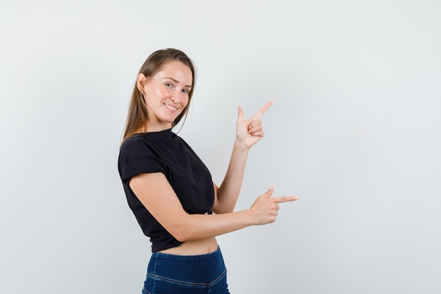 Mujer joven en blusa negra, pantalones haciendo gesto de pistola y mirando feliz