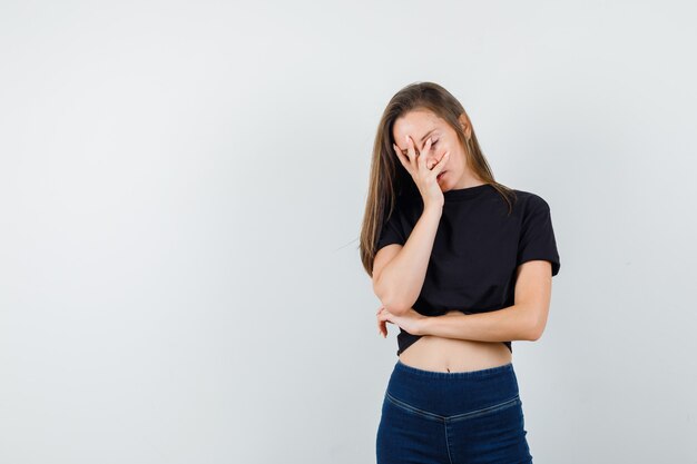 Mujer joven en blusa negra, pantalones sosteniendo la mano en la cara y con aspecto cansado