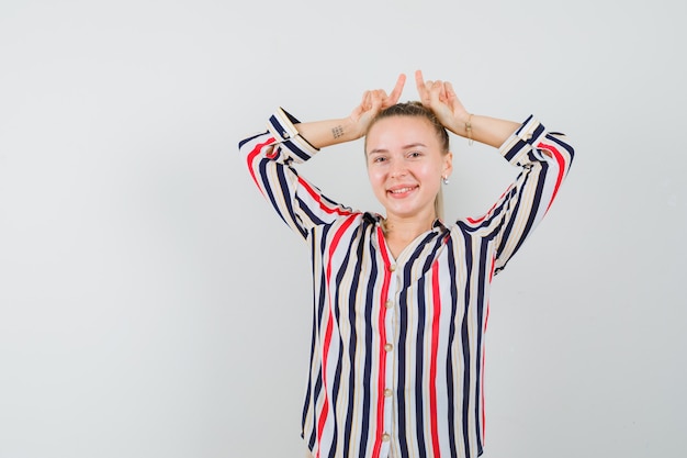 Mujer joven en blusa de rayas mostrando gesto de conejo y sonriendo y mirando feliz