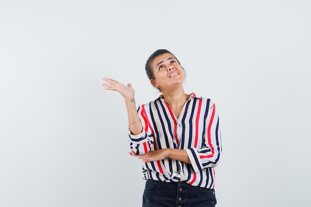 Mujer joven en blusa a rayas de pie en pose de escucha y tratando de mirar algo arriba y mirando enfocado