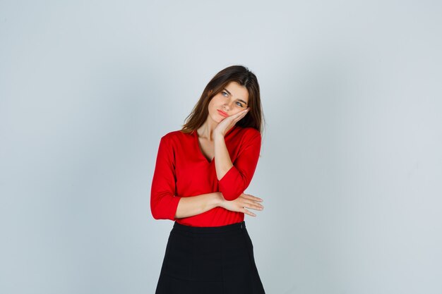 Mujer joven en blusa roja, falda negra apoyándose en la mejilla en la palma