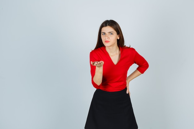 Mujer joven en blusa roja, falda negra estirando la mano