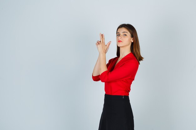 Mujer joven en blusa roja, falda negra mostrando gesto de pistola y mirando confiado