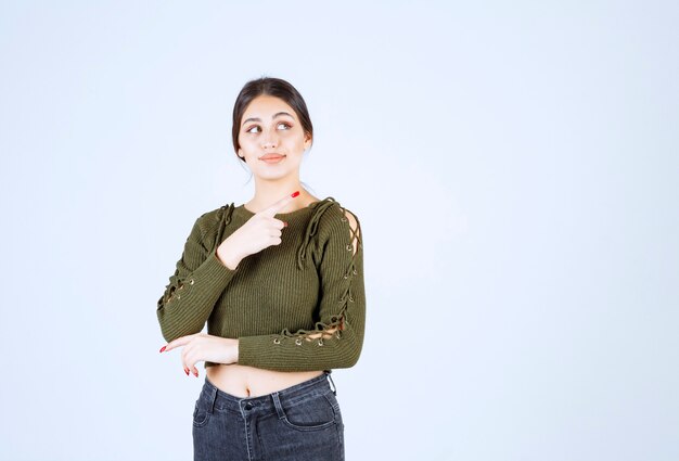 Mujer joven en blusa verde apuntando a algún lugar de la pared blanca