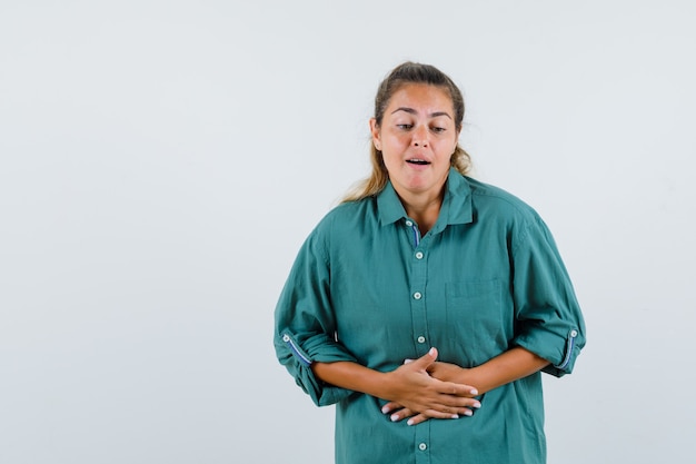 Mujer joven en blusa verde con dolor de estómago y mirando agotado