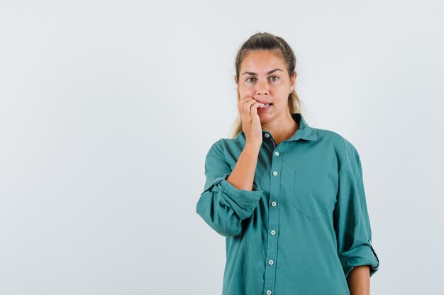 Mujer joven en blusa verde mordiendo los dedos y luciendo lindo