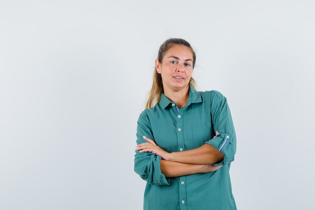 Mujer joven en blusa verde de pie con los brazos cruzados y mirando feliz