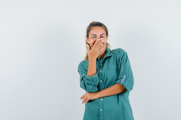 Mujer joven en blusa verde que cubre la boca con la mano mientras se ríe y se ve lindo