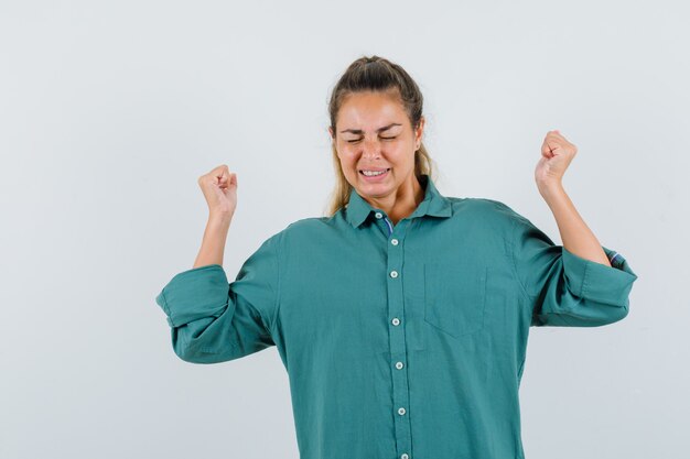 Mujer joven en blusa verde que muestra el gesto del ganador y parece optimista