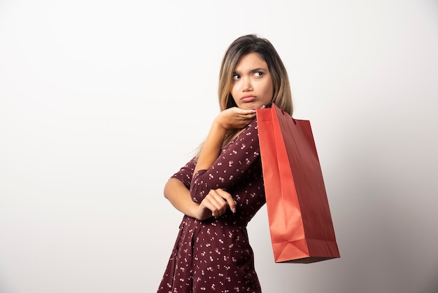 Mujer joven con bolsa de compras en la pared blanca.