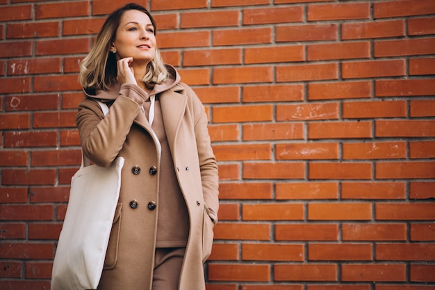 Foto gratuita mujer joven con bolsa junto a la pared de ladrillo