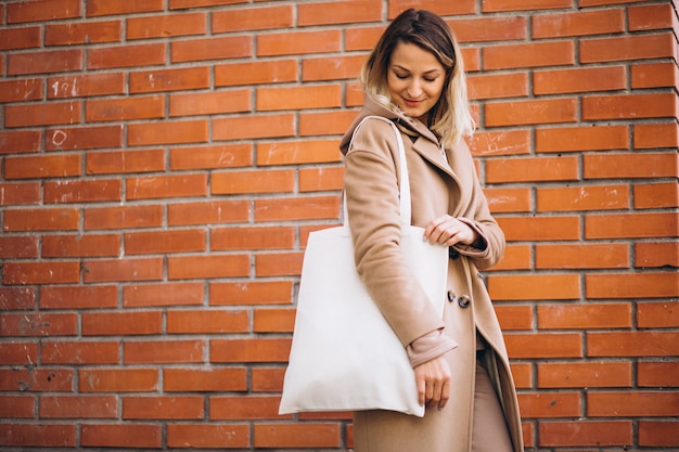 Mujer joven con bolsa junto a la pared de ladrillo