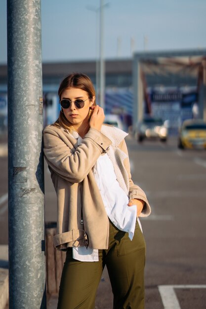 Mujer joven con bolsas de la compra en una parada de autobús posando para la cámara.