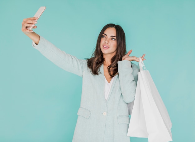 Mujer joven con bolsas de compras tomando un selfie