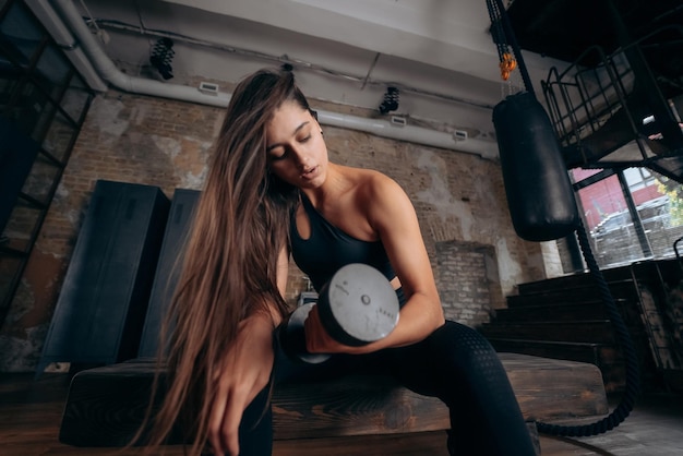 La mujer joven bombea los músculos con un brazo levantando pesas