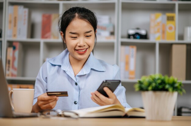 Mujer joven y bonita alegre con teléfono móvil, compras en línea y pago con tarjeta bancaria de crédito