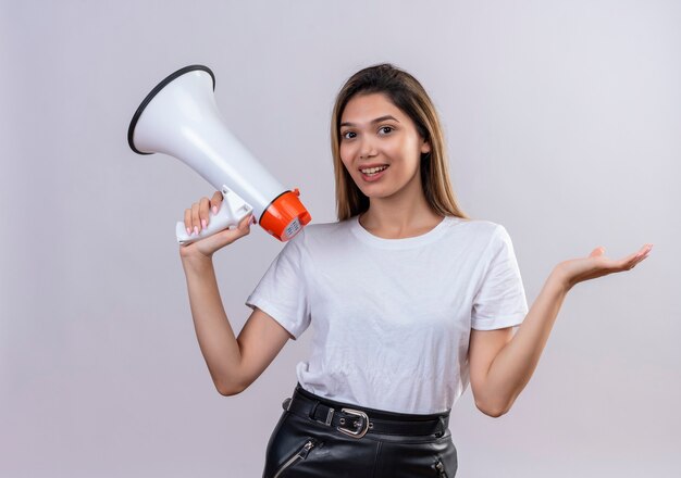 Una mujer joven y bonita en camiseta blanca con megáfono en una pared blanca