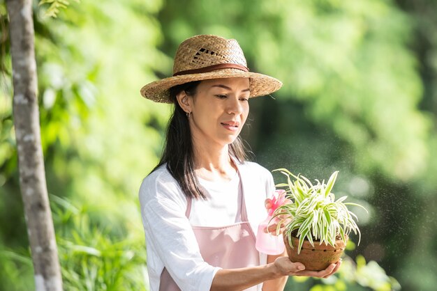 Mujer joven y bonita regar el árbol en el jardín en un día soleado de verano. mujer jardinería exterior en la naturaleza de verano. concepto de agricultura, jardinería, agricultura y personas.