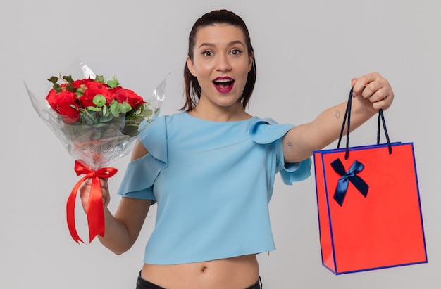 Mujer joven y bonita sorprendida con ramo de flores y bolsa de regalo