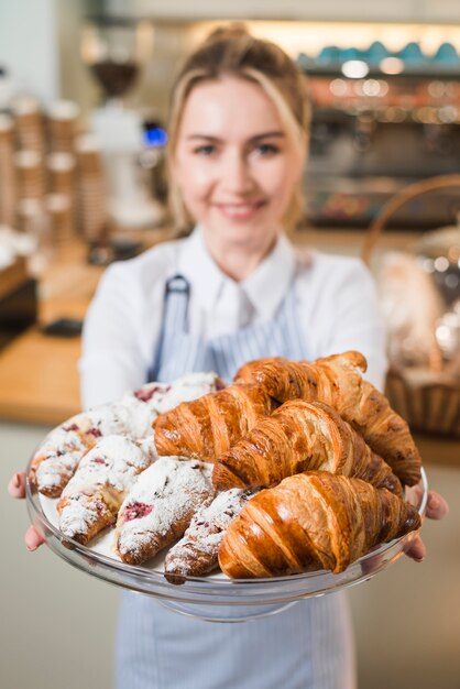 Mujer joven borrosa que ofrece los croissants en el soporte de la torta de cristal