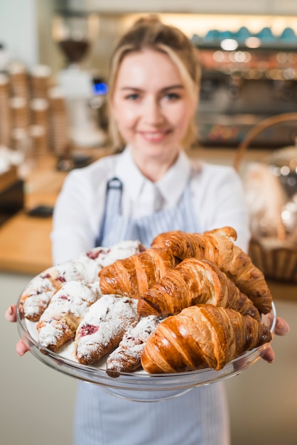 Mujer joven borrosa que ofrece los croissants en el soporte de la torta de cristal