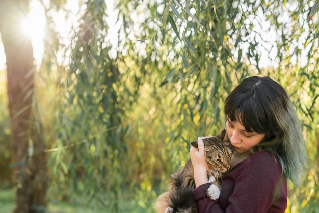 Foto gratuita mujer joven en el bosque que sostiene su gato de gato atigrado encantador