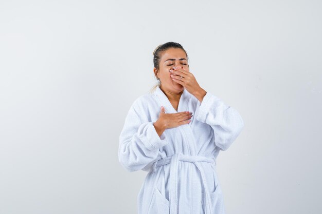 Mujer joven bostezando en bata de baño y mirando soñoliento