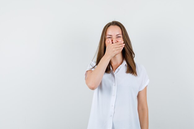 Mujer joven bostezando boca con su mano en blusa blanca y mirando hastiado