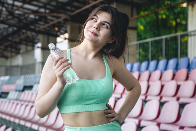 Una mujer joven con una botella de agua entrenando en el estadio