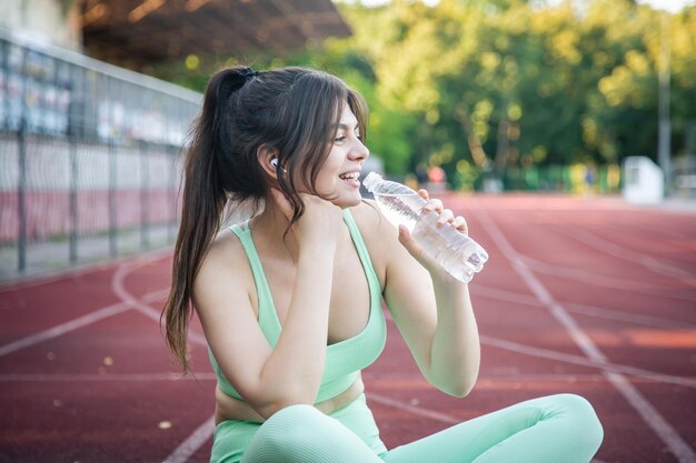 Una mujer joven con una botella de agua entrenando en el estadio