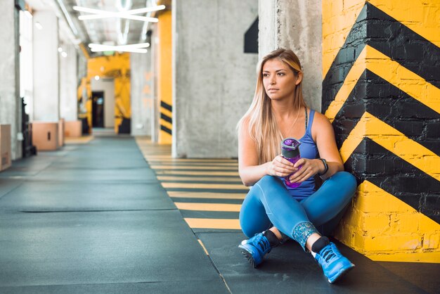 Mujer joven con botella de agua sentado en el gimnasio