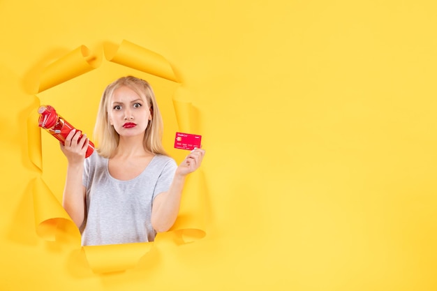 Mujer joven con botella roja y tarjeta de crédito sobre fondo amarillo deporte atleta gimnasio venta de dinero