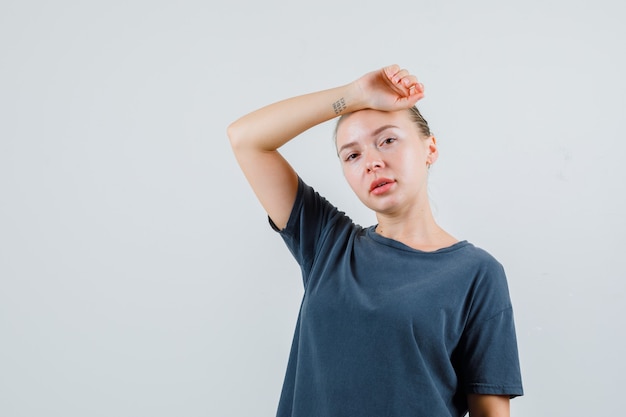 Mujer joven con el brazo levantado inclinado sobre la cabeza en camiseta gris y luciendo agradable