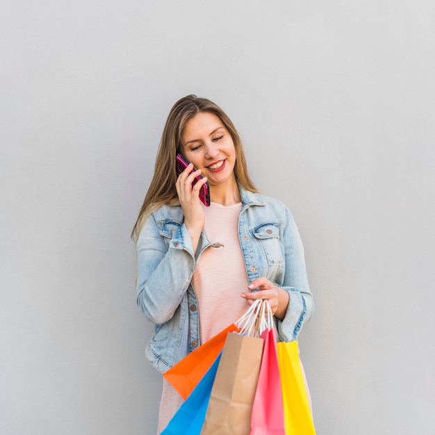 Mujer joven con brillantes bolsas de compras hablando por teléfono