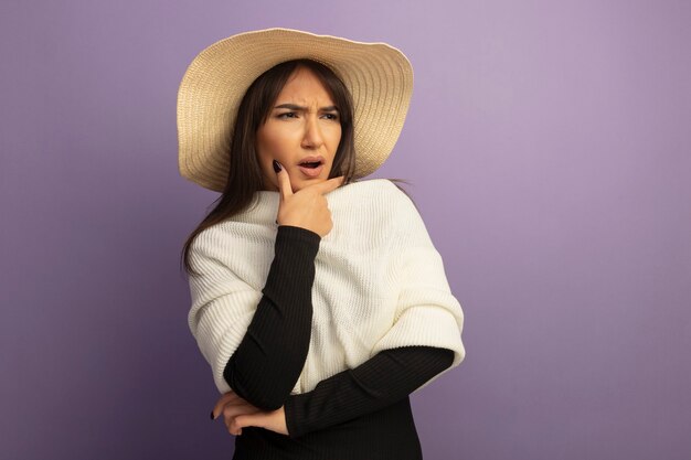 Mujer joven con bufanda blanca y sombrero de verano mirando a un lado confundido y disgustado