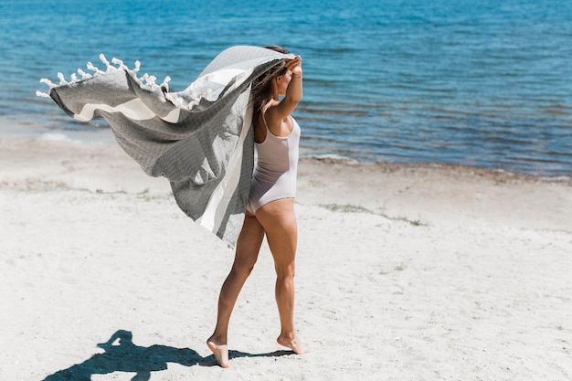 Mujer joven con bufanda caminando en la playa