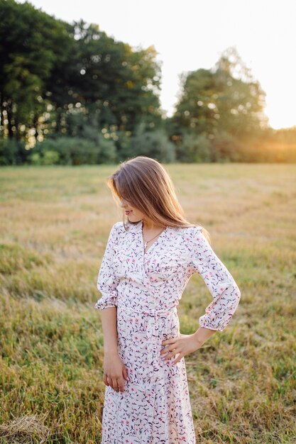 Mujer joven con un cabello hermoso posando en el campo al atardecer. Moda, independencia