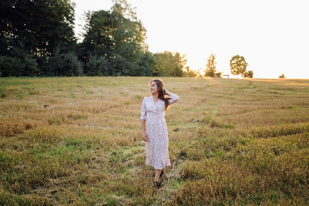 Mujer joven con un cabello hermoso posando en el campo al atardecer. Moda, independencia