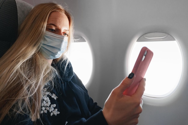 Mujer joven con cabello largo sentado en el avión junto a la ventana y con smartphone