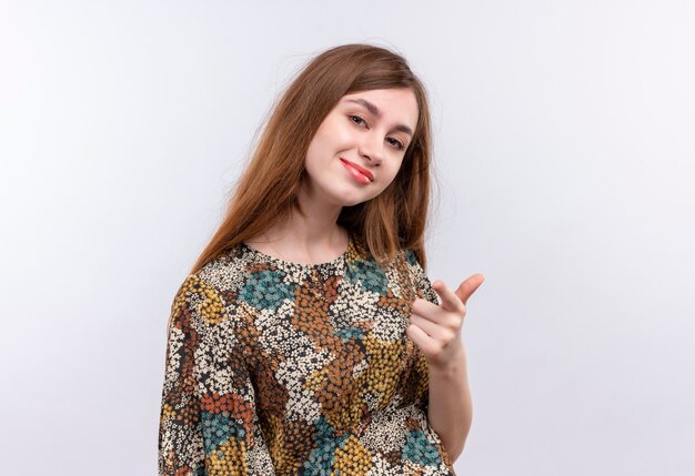 Mujer joven con cabello largo y vestido colorido sonriendo confiado, apuntando al frente