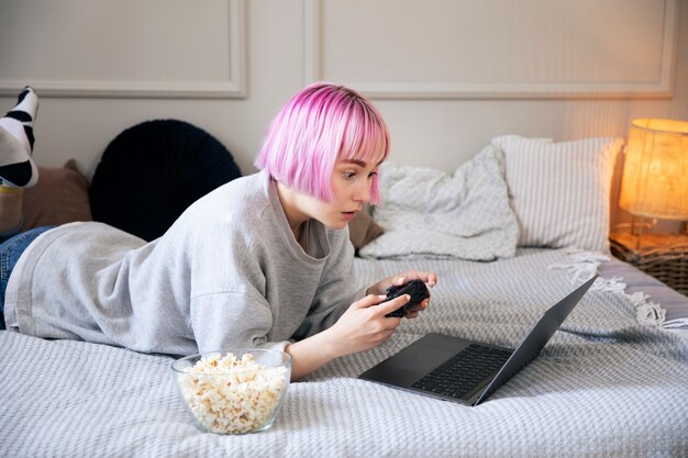 Mujer joven con cabello rosado jugando con un joystick en la computadora portátil