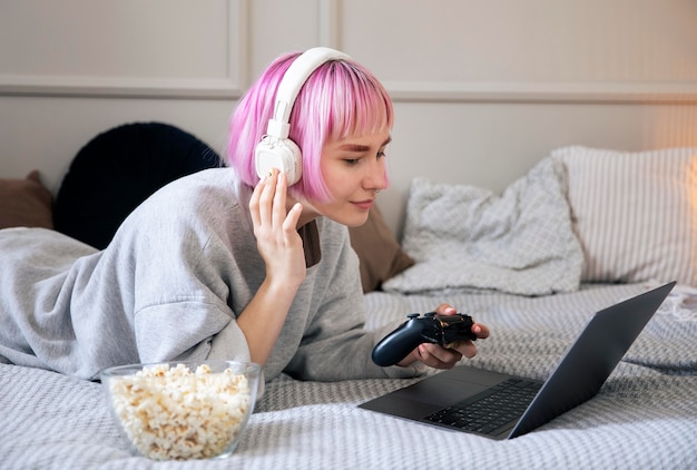 Mujer joven con cabello rosado jugando con un joystick en la computadora portátil