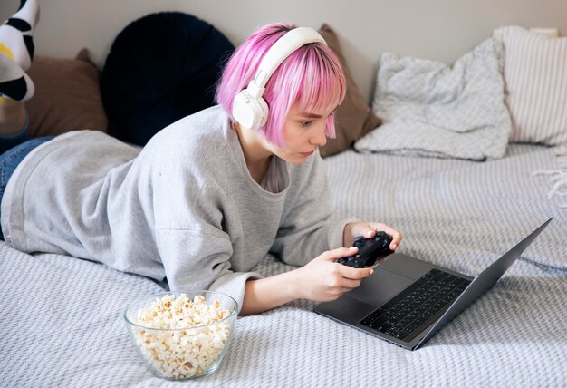 Mujer joven con cabello rosado jugando con un joystick en la computadora portátil