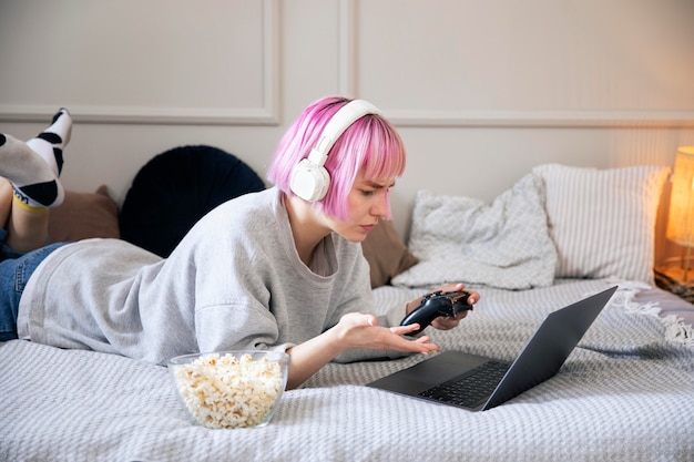 Mujer joven con cabello rosado jugando con un joystick en la computadora portátil